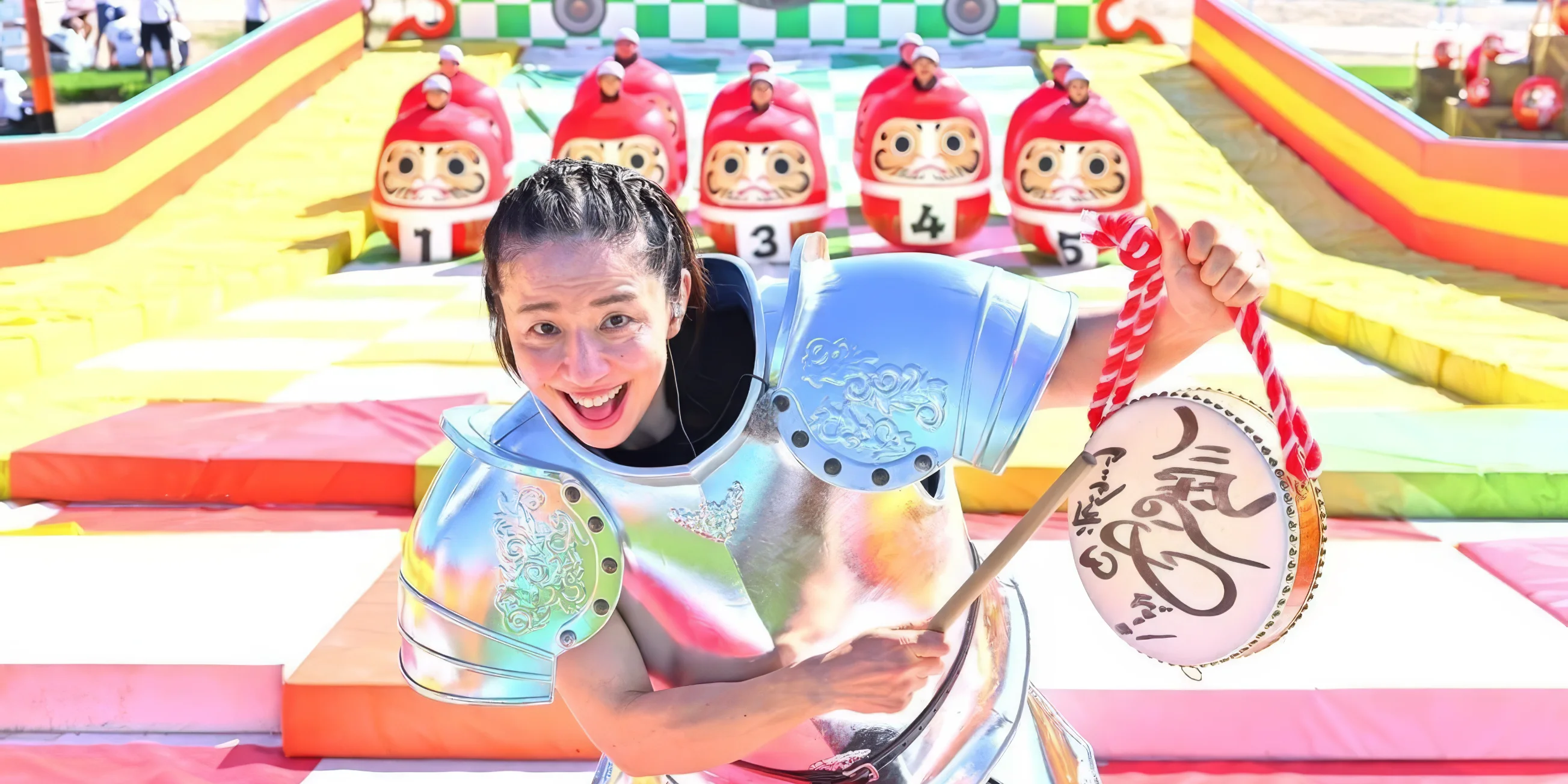 Guard Kyoko stands at the top of 'Blueberry Hill' with two rows of contestants dressed as giant darumas at the bottom of the slope behind her